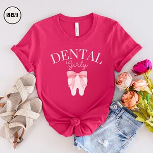 May include: Pink t-shirt with the text "DENTAL Girly" and a pink tooth with a pink bow on it.