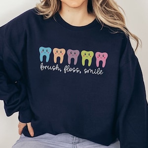 May include: A navy blue sweatshirt with a row of five colorful cartoon teeth and the text "brush, floss, smile".