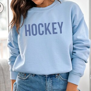 May include: A light blue sweatshirt with the word "HOCKEY" printed in a darker blue color on the front.