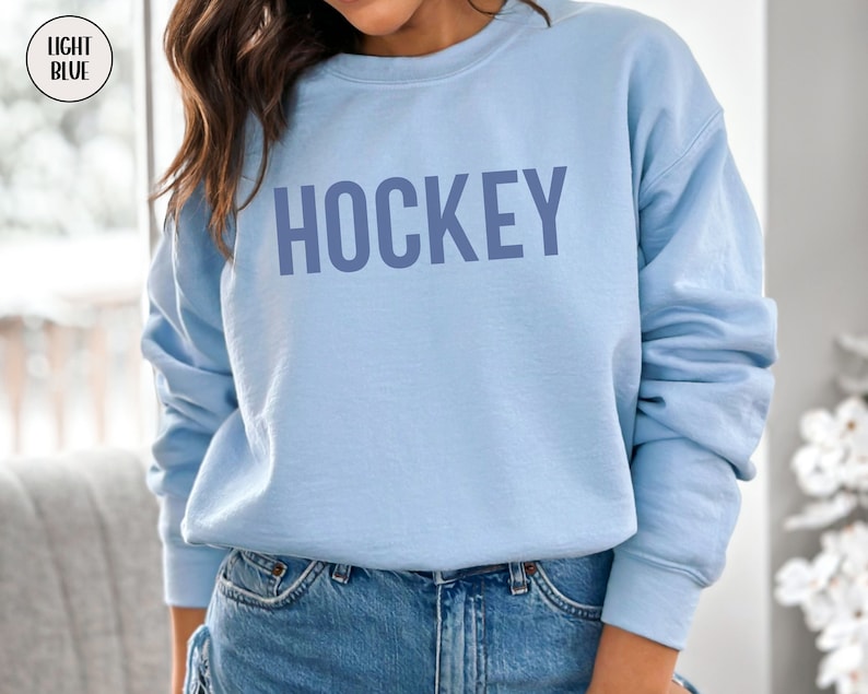 May include: A light blue sweatshirt with the word "HOCKEY" printed in a darker blue color on the front.