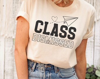 May include: A beige t-shirt with the text "CLASS DISMISSED" in black. A paper airplane with a heart is flying above the text.