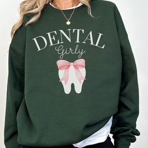 May include: A dark green sweatshirt with the text "DENTAL Girly" and a white tooth with a pink bow on it.