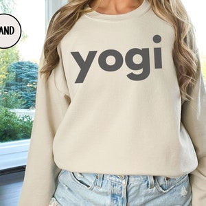 Może przedstawiać: Szarobrązowa bluza z nadrukiem słowa "yogi" w kolorze czarnym na przodzie.
