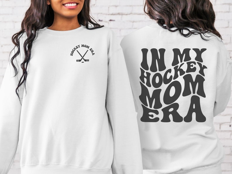 May include: White sweatshirt with a black graphic on the front that says "Hockey Mom Era" with crossed hockey sticks. The back of the sweatshirt has a black graphic that says "In My Hockey Mom Era" in a retro font.