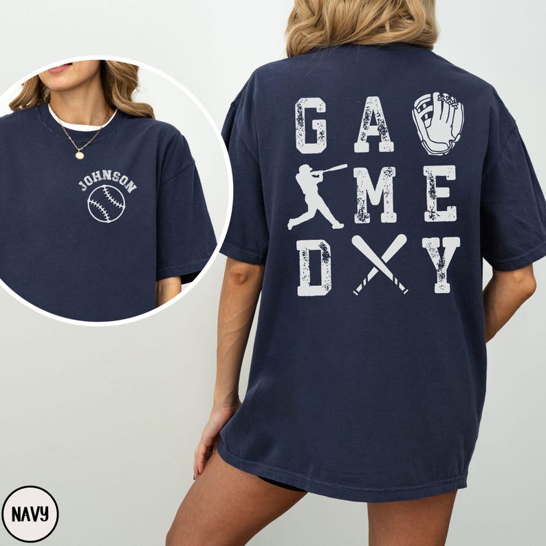 May include: Navy blue t-shirt with a white baseball graphic and the text "Johnson" on the front. The back of the shirt has a white graphic of a baseball player, bats, and a glove with the text "GAME DAY".