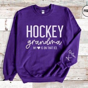 May include: Purple sweatshirt with the text "HOCKEY grandma MY &hearts; IS ON THAT ICE" and a hockey stick graphic on the sleeve. The text "Nolan" is also on the sleeve.