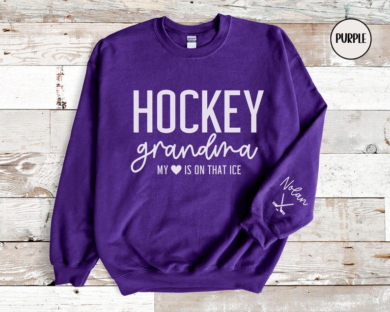 May include: Purple sweatshirt with the text "HOCKEY grandma MY &hearts; IS ON THAT ICE" and a hockey stick graphic on the sleeve. The text "Nolan" is also on the sleeve.