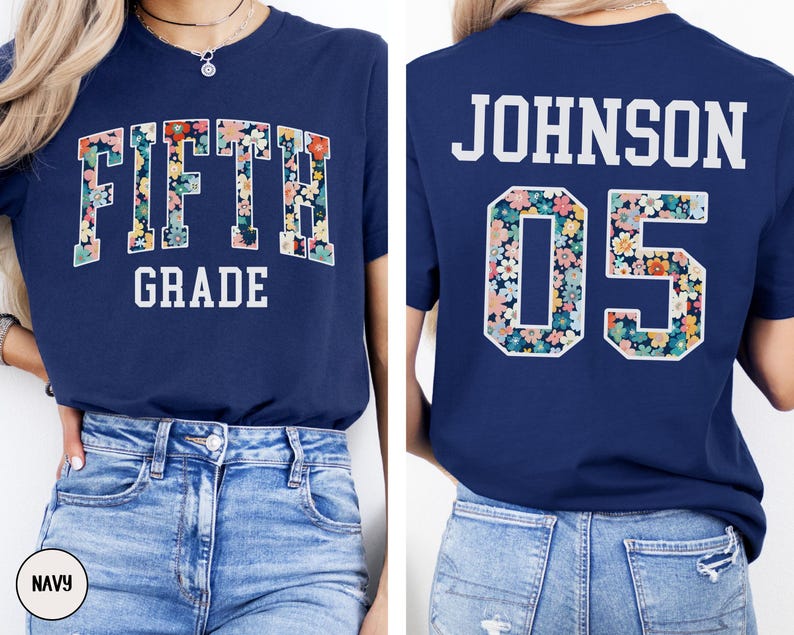 Op de afbeelding: Marineblauwe t-shirt met de tekst "FIFTH GRADE" in witte blokletters. Het woord "FIFTH" is gevuld met een bloemenpatroon. De achterkant toont de naam "JOHNSON" en het nummer "05" in een bloemenpatroon.