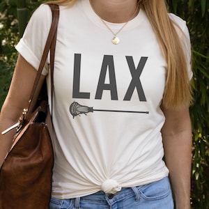 May include: White t-shirt with a black graphic of a lacrosse stick and the word "LAX" printed on it.