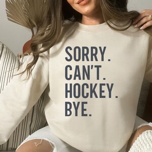 May include: A white sweatshirt with the text "SORRY. CAN'T. HOCKEY. BYE." printed in dark blue.