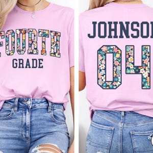 May include: A light pink t-shirt with the words "FOURTH GRADE" in a floral design on the front. The back of the shirt has the name "JOHNSON" and the number "04" in a floral design.