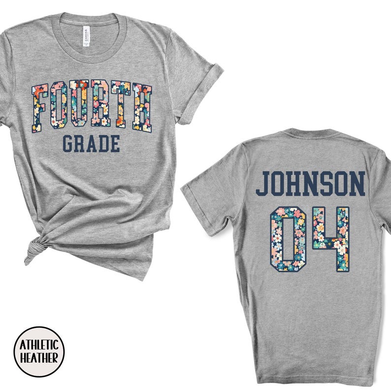 May include: A heather gray t-shirt with "FOURTH GRADE" in a floral design on the front. The back of the shirt displays "JOHNSON" and the number "04" in a floral pattern. The shirt is made of athletic heather material.