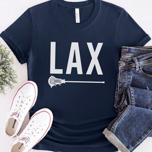 May include: A navy blue t-shirt with a white graphic of a lacrosse stick and the word "LAX" printed on the front.
