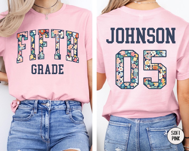 Op de afbeelding: Een lichtroze t-shirt met de woorden "FIFTH GRADE" in een bloemenpatroon. De achterkant van de shirt heeft de naam "JOHNSON" en het nummer "05" in een bloemenpatroon. Het shirt is gemaakt van een zacht materiaal.