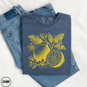 Op de afbeelding: Een marineblauw t-shirt met een gele citroenprint. De citroen is omringd door bladeren en bloemen. Het t-shirt is gemaakt van een zacht, comfortabel materiaal.