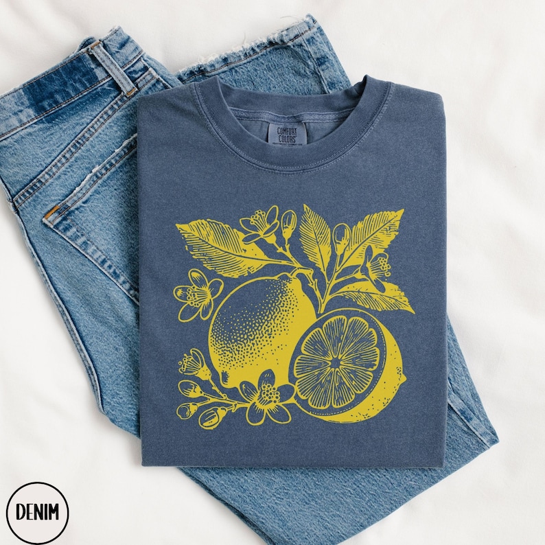 Op de afbeelding: Een marineblauw t-shirt met een gele citroenprint. De citroen is omringd door bladeren en bloemen. Het t-shirt is gemaakt van een zacht, comfortabel materiaal.