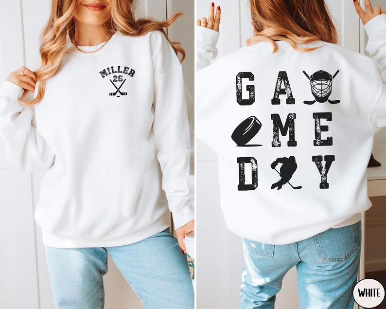 May include: White sweatshirt with a black hockey-themed design on the front and back. The front design says "Miller 26" with crossed hockey sticks. The back design says "GAME DAY" with a hockey puck, a hockey player, and a hockey mask.
