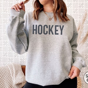 May include: A gray sweatshirt with the word "HOCKEY" printed in black on the front. The sweatshirt is a relaxed fit and has a crew neck.