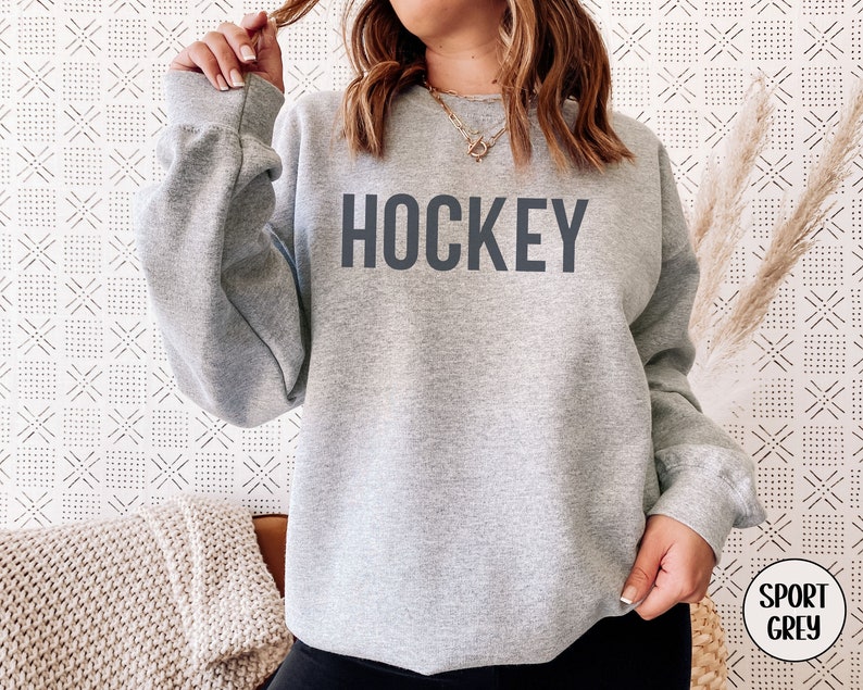 May include: A gray sweatshirt with the word "HOCKEY" printed in black on the front. The sweatshirt is a relaxed fit and has a crew neck.