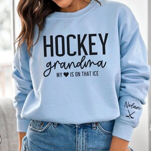 May include: Light blue sweatshirt with the text "Hockey grandma my heart is on that ice" and a hockey stick graphic on the sleeve. The text "Nolan" is also on the sleeve.