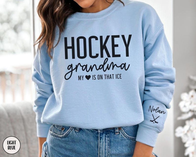 May include: Light blue sweatshirt with the text "Hockey grandma my heart is on that ice" and a hockey stick graphic on the sleeve. The text "Nolan" is also on the sleeve.