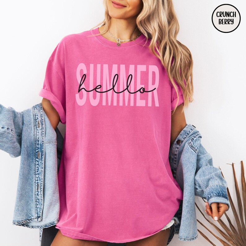 May include: A bright pink t-shirt with the word "SUMMER" in light pink block letters and the word "hello" in black cursive script. The shirt is part of a summer clothing collection.