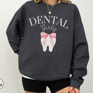 May include: Dark heather grey sweatshirt with the text "Dental Girly" and a pink bow on a white tooth graphic.