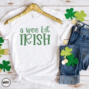 以下が含まれることがあります： 緑色の「a wee bit IRISH」という文字が入った白いTシャツ。青いジーンズ、金貨、緑のクローバーの装飾が施されており、聖パトリックの日に最適です。