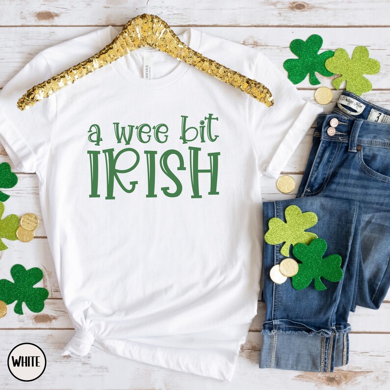 以下が含まれることがあります： 緑色の「a wee bit IRISH」という文字が入った白いTシャツ。青いジーンズ、金貨、緑のクローバーの装飾が施されており、聖パトリックの日に最適です。