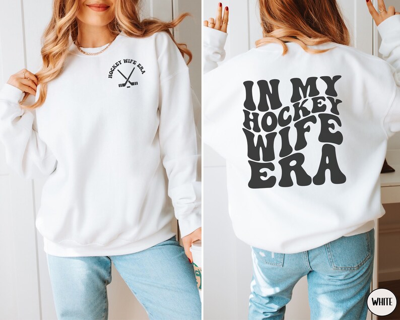 Pu&ograve; includere: Felpa bianca con il testo "In My Hockey Wife Era" in un font retr&ograve; sul retro e una piccola grafica di bastone da hockey sul davanti.