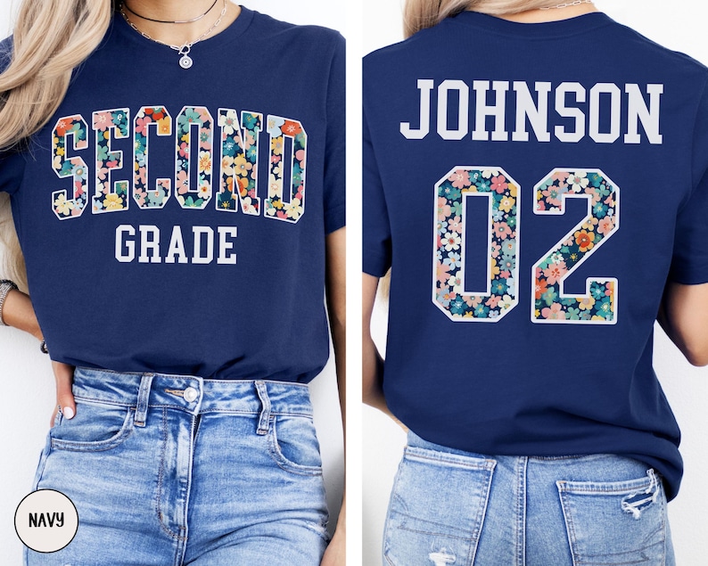 Puede incluir: Camiseta azul marino con "SECOND GRADE" en letras florales en la parte delantera. La parte trasera muestra "JOHNSON 02" con n&uacute;meros estampados florales. Una prenda casual con tem&aacute;tica escolar.