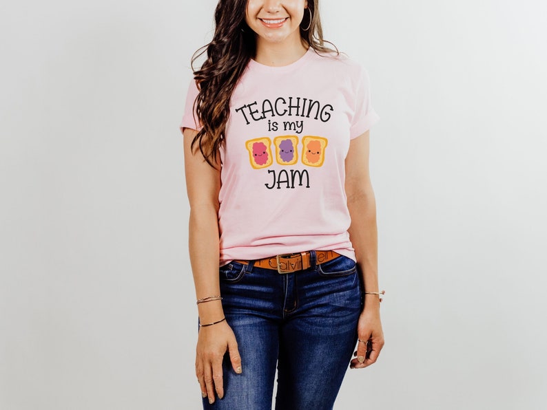 Peut inclure: Un t-shirt rose avec le texte "TEACHING is my JAM" et un graphique de trois tranches de pain grill&eacute; avec de la gel&eacute;e de diff&eacute;rentes couleurs.