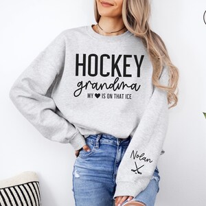 May include: Gray sweatshirt with the text "HOCKEY grandma MY &hearts; IS ON THAT ICE" and the name "Nolan" printed on the sleeve with a hockey stick graphic.