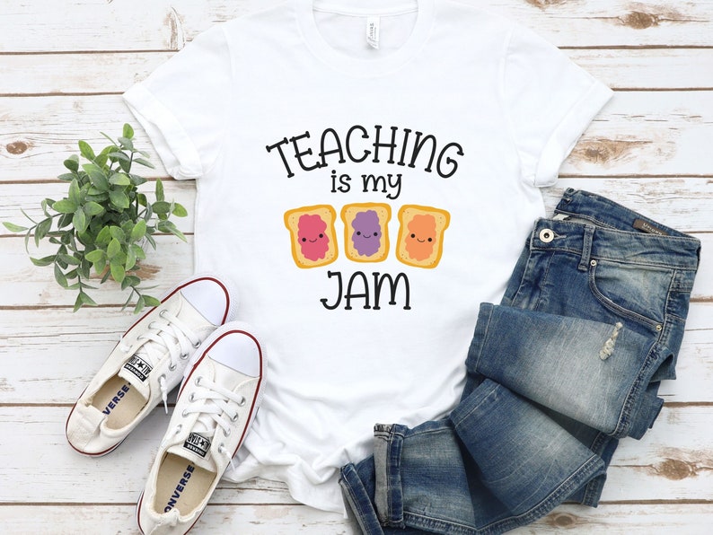 Peut inclure: T-shirt blanc avec le texte "TEACHING is my JAM" et trois images de toasts de dessin anim&eacute; avec de la gel&eacute;e de diff&eacute;rentes couleurs. Le toast a un visage heureux.