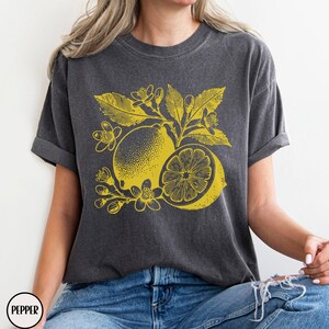 Op de afbeelding: Een donkergrijs T-shirt met een gele citroenprint. De print toont een citroen met bladeren en bloemen.