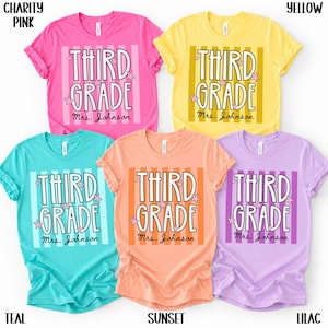 May include: Five short-sleeved crew neck t-shirts in charity pink, yellow, teal, sunset, and lilac. Each shirt features vertical stripes and the text "THIRD GRADE" with small star accents and the personalized name "Mrs. Johnson" printed below.