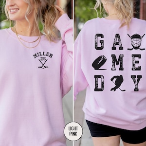 May include: Light pink sweatshirt with the text "GAME DAY" on the back and a hockey stick and puck graphic. The front of the sweatshirt has the text "MILLER 26" with a hockey stick graphic.