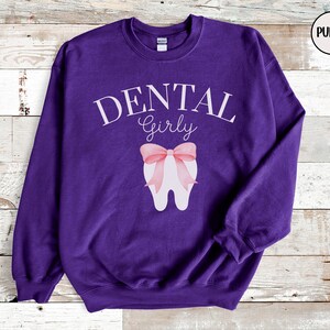 May include: Purple sweatshirt with the text "DENTAL Girly" and a white tooth with a pink bow on it.