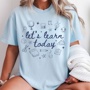 May include: Light blue t-shirt with a graphic design of school supplies and the text "let's learn today".