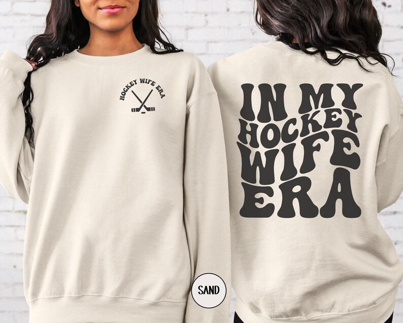Pu&ograve; includere: Una felpa color crema con la scritta "Hockey Wife Era" in nero sul retro. Il testo &egrave; in un font retr&ograve;. La parte anteriore della felpa ha un piccolo grafico nero di bastoni da hockey incrociati con un disco.