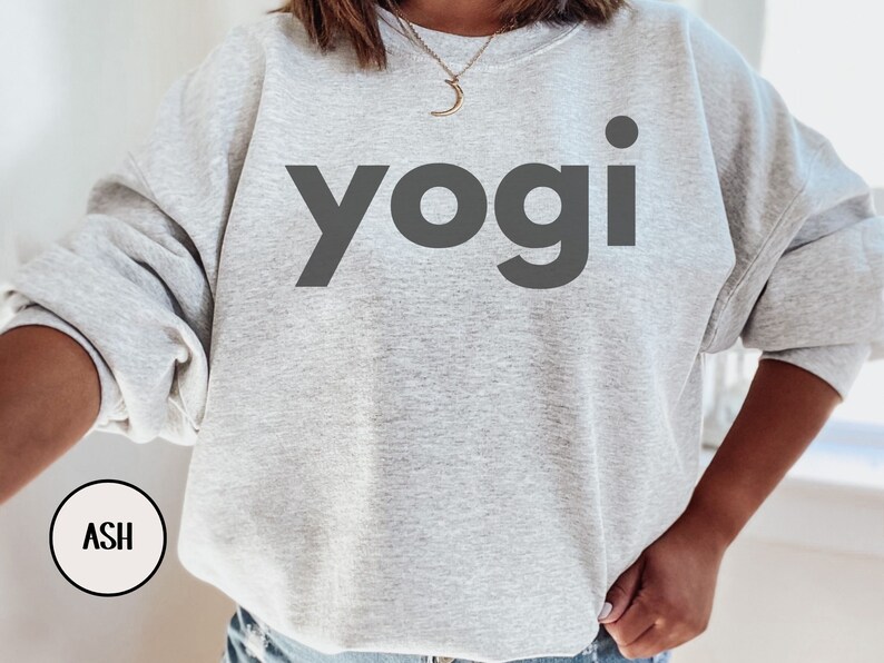 Może przedstawiać: Szara bluza z nadrukiem słowa "yogi" w kolorze czarnym na przodzie. Bluza wykonana jest z miękkiego, wygodnego materiału i ma luźny kr&oacute;j.