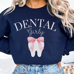 May include: Navy blue sweatshirt with the text "Dental Girly" and a white tooth with a pink bow.