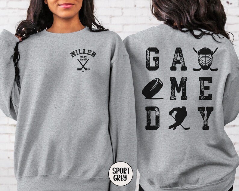 May include: Gray sweatshirt with the text "GAME DAY" in black with hockey-themed graphics. The back of the sweatshirt has the text "MILLER 26" with crossed hockey sticks.