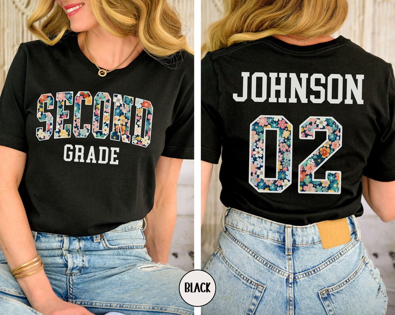 Puede incluir: Camiseta negra con las palabras "SECOND GRADE" en un dise&ntilde;o floral en la parte delantera. La parte trasera de la camiseta muestra el nombre "JOHNSON" y el n&uacute;mero "02" en un patr&oacute;n floral. La camiseta se usa con vaqueros azules.