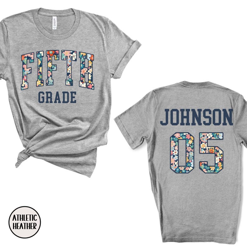 Op de afbeelding: Athletic heather grijze t-shirts met bloemenprint tekst. De voorkant van het shirt zegt "FIFTH GRADE" in een bloemenontwerp. De achterkant van het shirt heeft "JOHNSON 05" in een bloemenontwerp. Het shirt is gemaakt van een zacht materiaal.