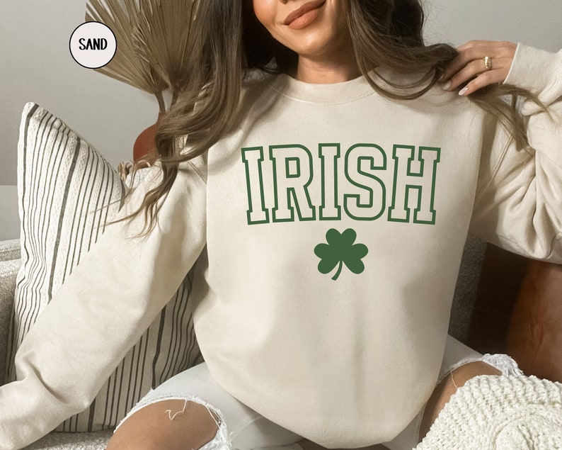 Op de afbeelding: Een cr&egrave;mekleurig sweatshirt met het woord "IRISH" in groen met een witte omlijsting. Onder het woord staat een groen klavertje vier.