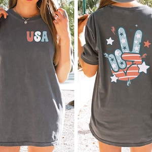 May include: A dark gray t-shirt with a red, white, and blue peace sign graphic on the back and the word "USA" in colorful letters on the front.