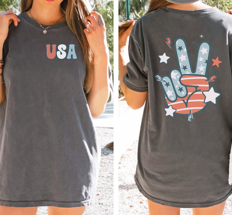 May include: A dark gray t-shirt with a red, white, and blue peace sign graphic on the back and the word "USA" in colorful letters on the front.