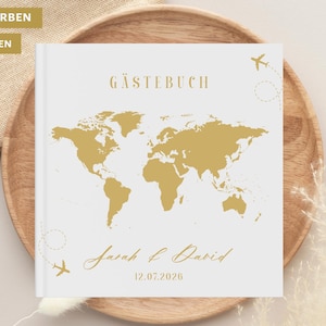 May include: A white guest book with a gold world map design. The book features the word "Gästebuch" at the top and the names "Sarah & David" with the date "12.07.2026" below the map. Two small airplane illustrations are also present.
