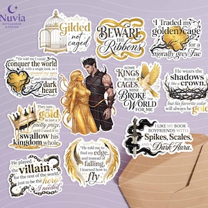 May include: A collection of fantasy-themed stickers with gold and black designs. The stickers feature quotes, illustrations of a couple, a bird, a crown, and a sword. The text includes phrases like "Beware the Ribbons" and "I like my book boyfriends."